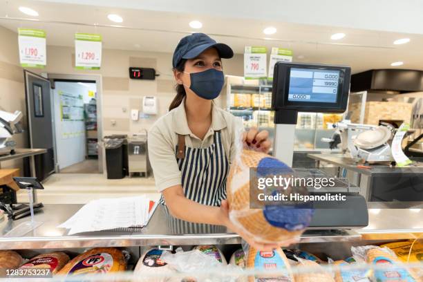 vrouw die bij een delicatessenwinkel werkt die een facemask draagt terwijl het verkopen van koud vlees - kalkoen witvlees stockfoto's en -beelden