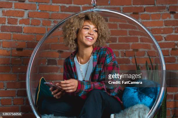 de jonge vrouw lacht en controleert telefoon - egg chair stockfoto's en -beelden