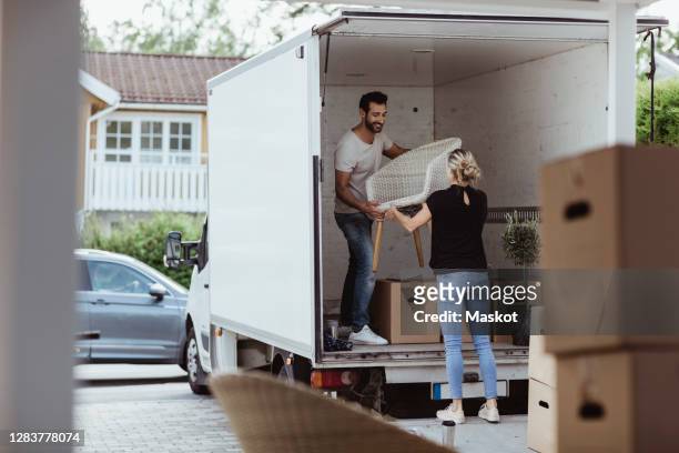 smiling male and female partners unloading chair from van - déménagement photos et images de collection