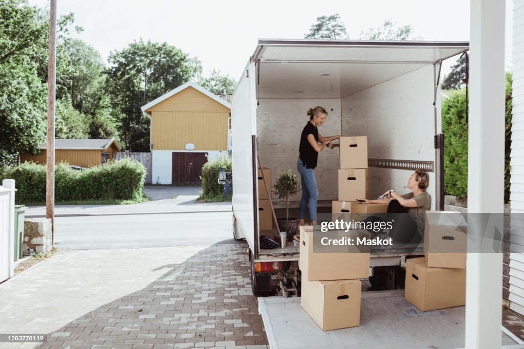Side view of woman with boxes talking to female friend in moving van