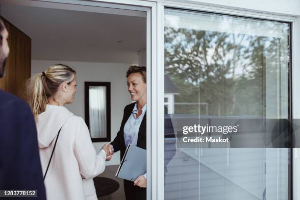 smiling female real estate agent greeting couple in new house - house showing stock pictures, royalty-free photos & images