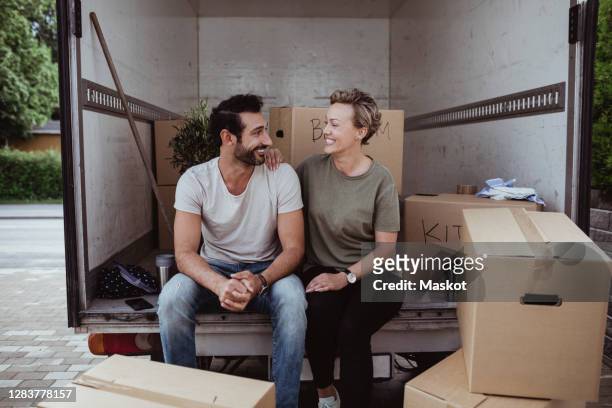 smiling male and female partners looking at each other while sitting by cardboard boxes in van - moving house stock pictures, royalty-free photos & images