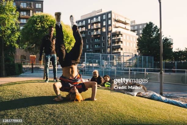 male friends looking at young man doing backflipping in field - headstand ストックフォトと画像