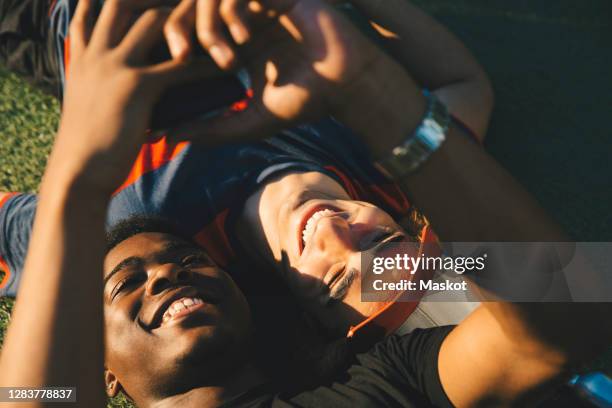 high angle view of smiling friends using smart phone while lying in park - stockholm park stock pictures, royalty-free photos & images