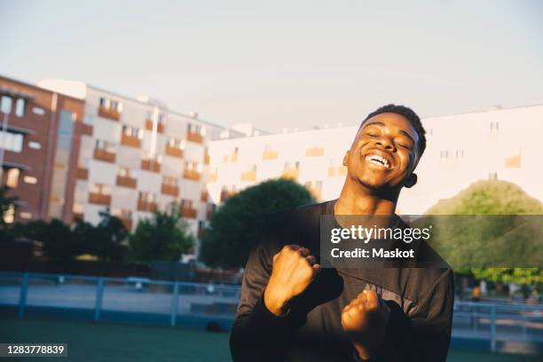 happy young man cheering with eyes closed in sports field - mann freundlich sport stock-fotos und bilder