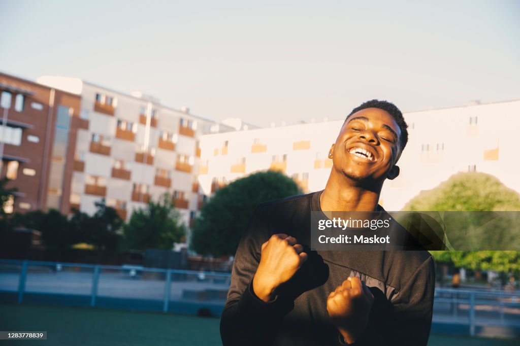 Happy young man cheering with eyes closed in sports field
