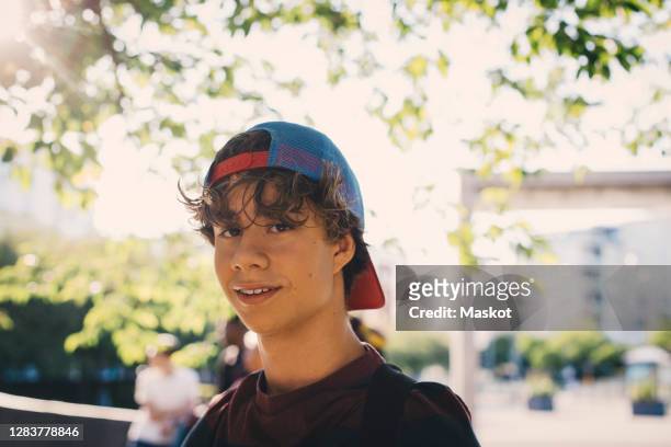 portrait of smiling male teenager wearing cap in park - teenage boy in cap posing stock pictures, royalty-free photos & images