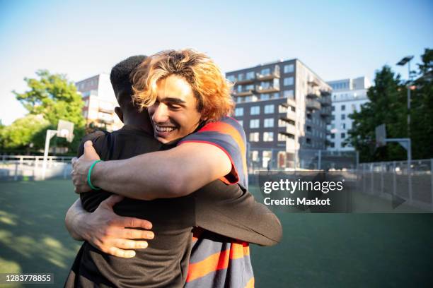 happy friends embracing each other while playing in sports field - man embracing stock pictures, royalty-free photos & images