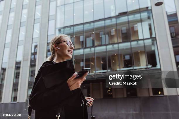 low angle view of businesswoman talking through in-ear headphones in city - businesswoman talking smartphone stock-fotos und bilder