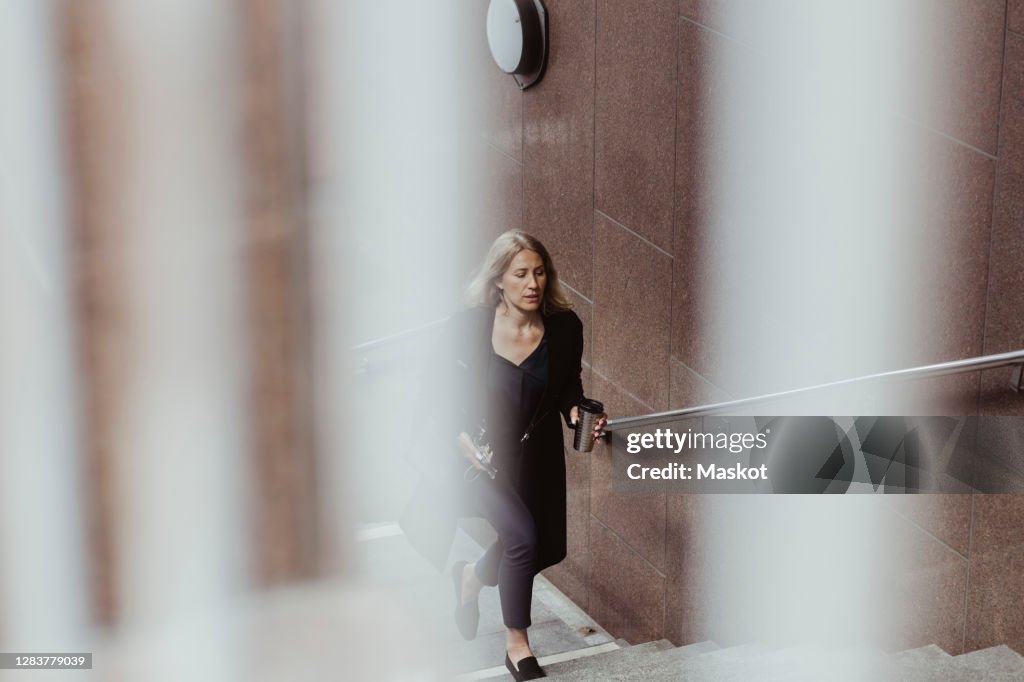 Businesswoman with coffee cup climbing staircase in city