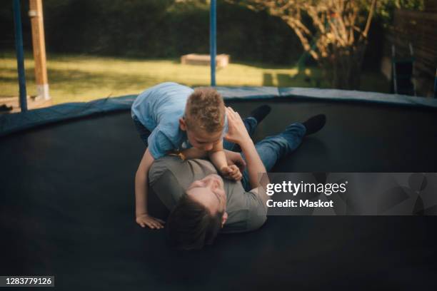 smiling father and son playing in trampoline during summer - boys wrestling stock pictures, royalty-free photos & images