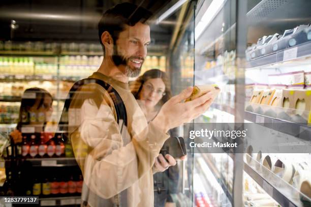 smiling customer reading ingredients while shopping with family in supermarket - supermarket refrigeration stock-fotos und bilder