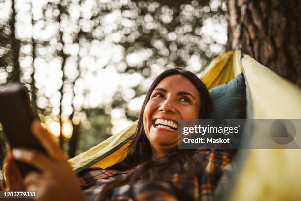 woman using smart phone while lying over hammock in forest - woman smartphone nature stockfoto's en -beelden