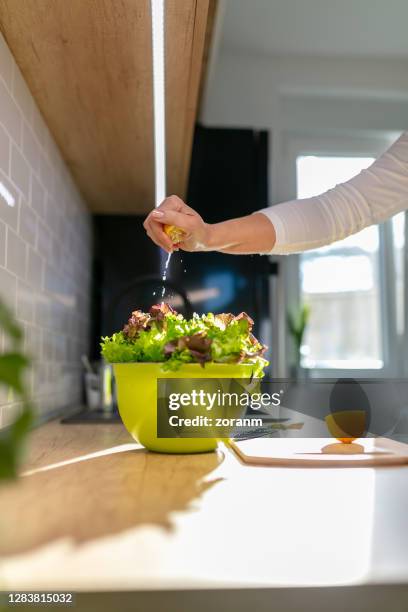 squeezing lemon on lettuce in a bowl on kitchen counter - leaf lettuce stock pictures, royalty-free photos & images