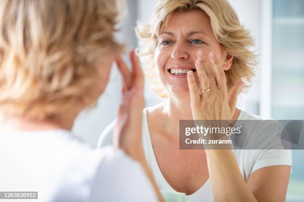 blonde frau reflexion im spiegel, lächelnd und berühren ihr gesicht - beautiful women spreading stock-fotos und bilder