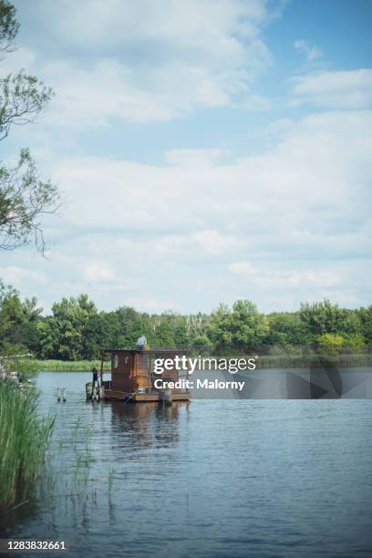 houseboat floating on river, man fishing from the rooftop. - hausboot stock-fotos und bilder