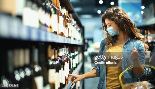 junge frau kauft während der coronavirus-pandemie im supermarkt wein - brown hair drink wine stock-fotos und bilder