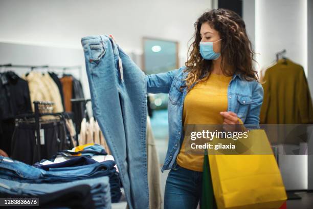young woman buying some jeans at a shopping mall after reopening. - denim store stock pictures, royalty-free photos & images