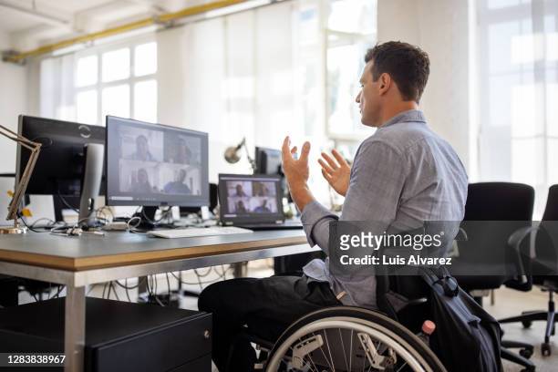 businessman with disability having a video call at his desk - wheelchair stock pictures, royalty-free photos & images