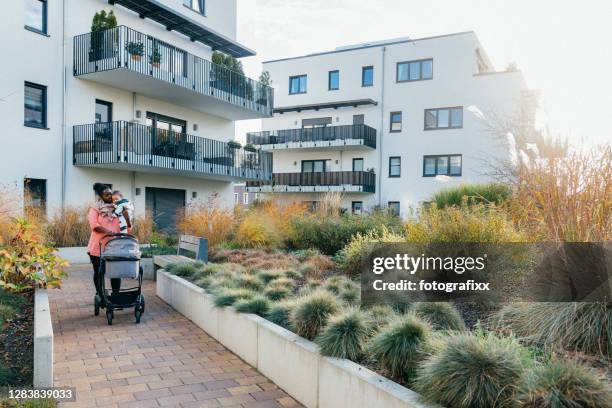 mother pushes her stroller on a path through townhouses - townhouse stock pictures, royalty-free photos & images