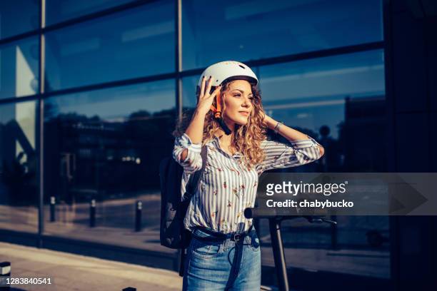 smiling woman puts crash helmet - electric push scooter stock pictures, royalty-free photos & images
