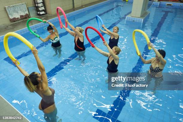 senior weibliche kunden mit einer nudel schwimmt während der hydrotherapie, so dass sie gleichgewicht haben können - aquarobics stock-fotos und bilder