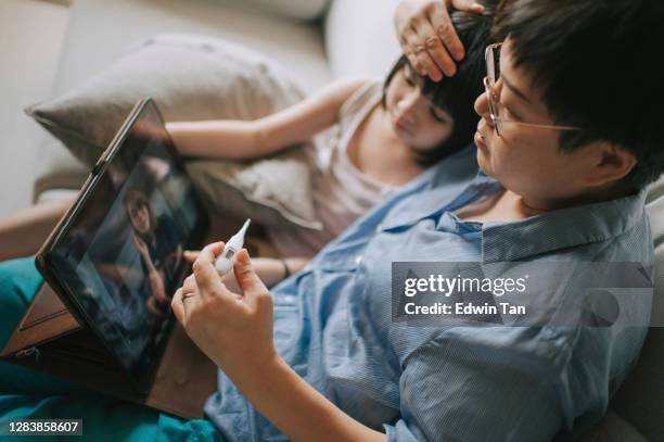 telemedicine telehealth aziatische chinese moeder met behulp van digitale tablet communiceren met arts kinderarts op haar dochter ziekte na het nemen van haar dochter temperatuur - mother daughter webcam stockfoto's en -beelden