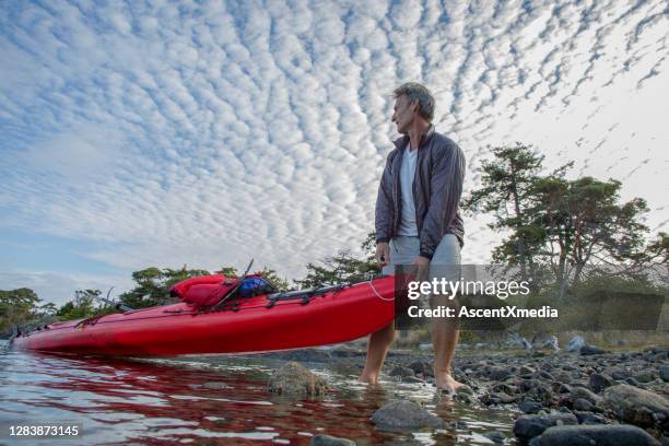 man pulls kayak from water on rocky beach - early retirement stock pictures, royalty-free photos & images