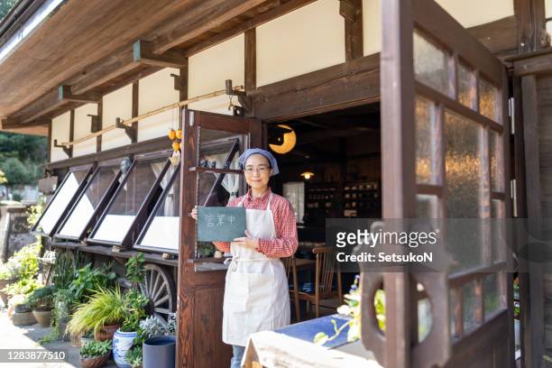 日本語で書かれた黒板の看板を持つアジアの古家カフェオーナー「we are open」。 - retail occupation ストックフォトと画像