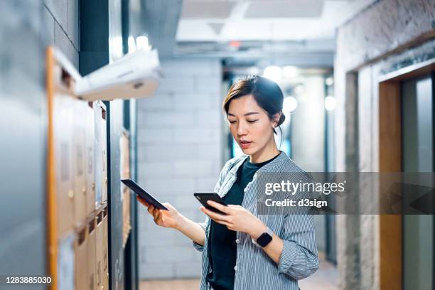 young asian female start-up business owner checking smartphone while collecting mails from mailbox in her shared office - hong kong post office photos et images de collection