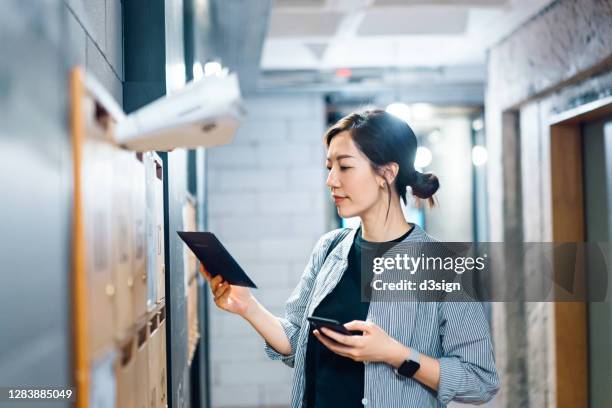 young asian female start-up business owner collecting mails from mailbox in her shared office - hong kong post office photos et images de collection