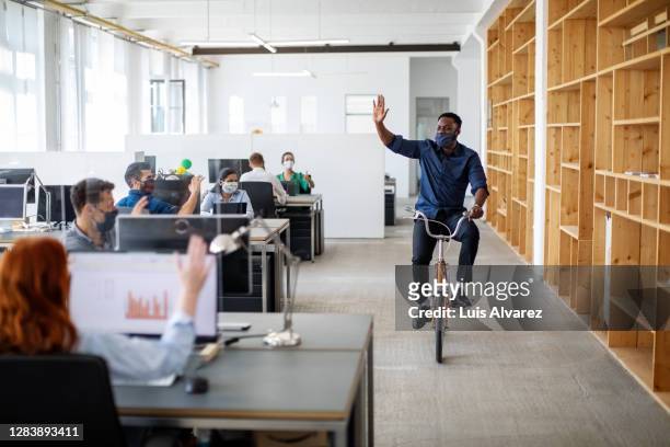 man waving hand to colleagues while riding a bicycle in office - reopening ceremony stock pictures, royalty-free photos & images