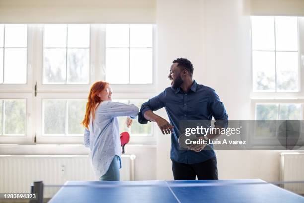 colleagues giving elbow bump while playing table tennis in office - schlägersport stock-fotos und bilder