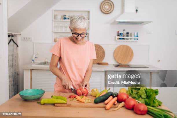 portrait of a happy senior woman chopping vegetables at her kitchen - chop stock pictures, royalty-free photos & images