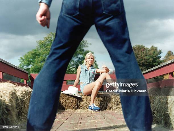 blonde woman, 24 years old, sitting on haybales facing a pair of man's legs in jeans, sherwood farms in easton, connecticut - hayride foto e immagini stock