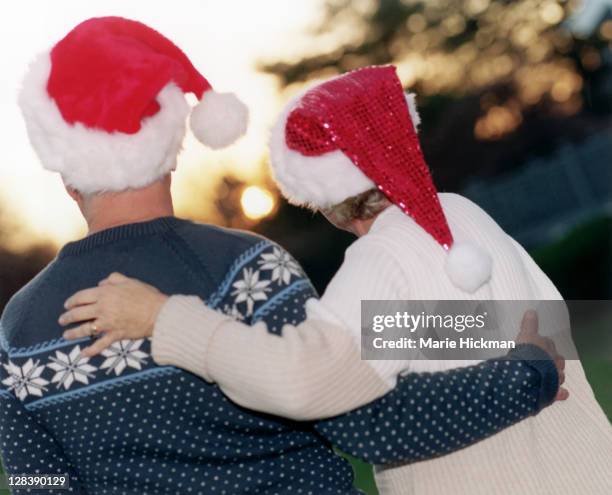 view from behind of a man, 64 old man, and 60 year old woman with santa hats at sunset. - 60 year old women stock-fotos und bilder