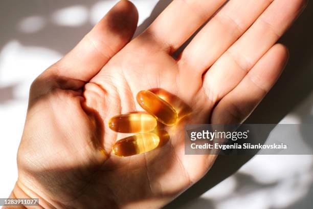woman's hand holding fish oil supplements on white background. - fish oil foto e immagini stock
