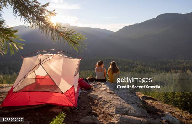 mujeres jóvenes ven la puesta de sol en un camping de cornisa de montaña - acampar fotografías e imágenes de stock
