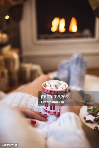 jeune belle femme buvant le chocolat chaud dans une atmosphère confortable de noël - chaussette noel cheminée photos et images de collection