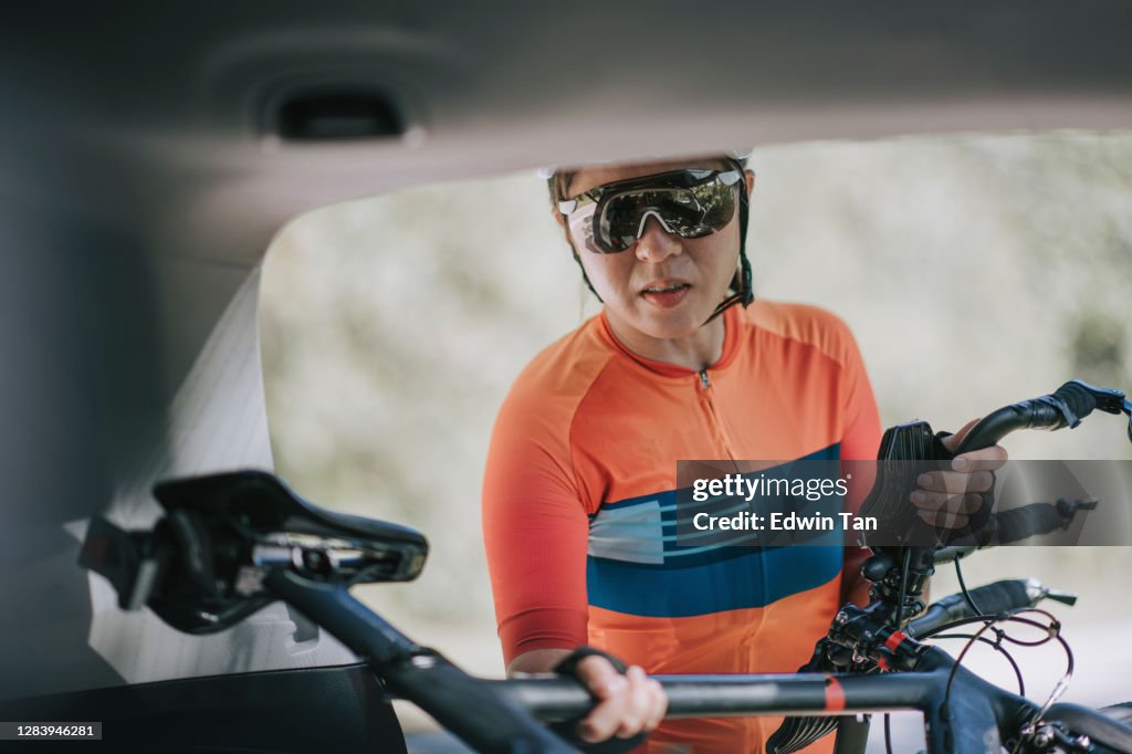 Asian chinese woman professional cyclist taking down her bicycle from the SUV car trunk ready to cycle