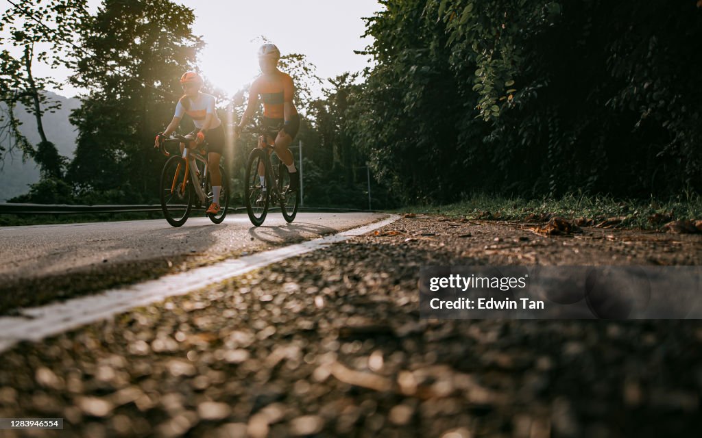 Low angle 2 asian chinese woman road cyclist side by side  cycling in rural area in the morning