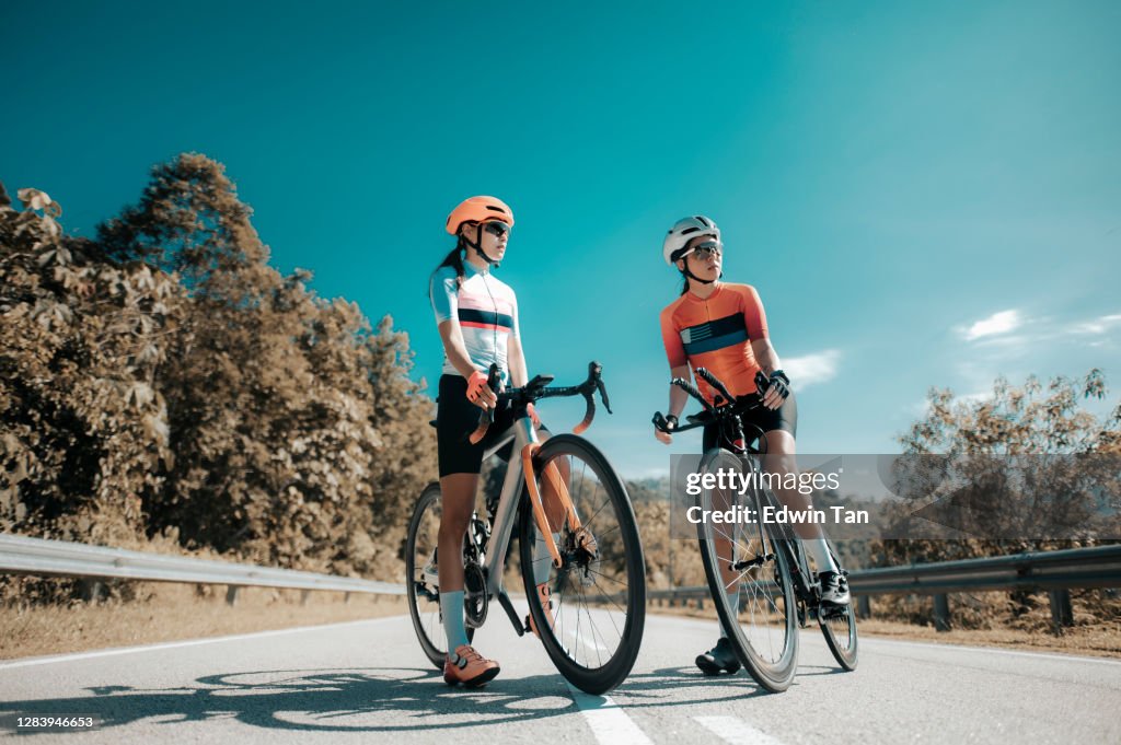 Asian chinese woman road bike cyclist leaning on road divider resting