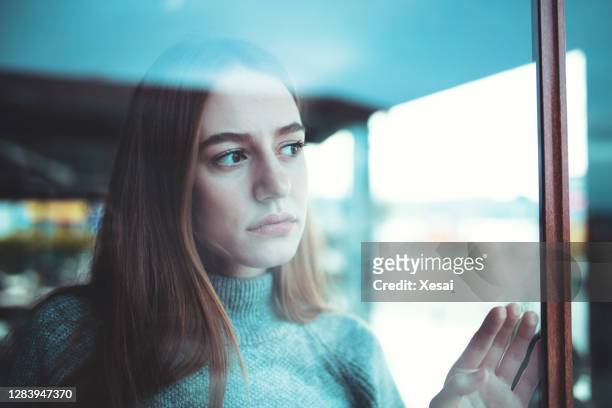 sad lonely young woman looking thoughtfully through window - suspicion stock pictures, royalty-free photos & images