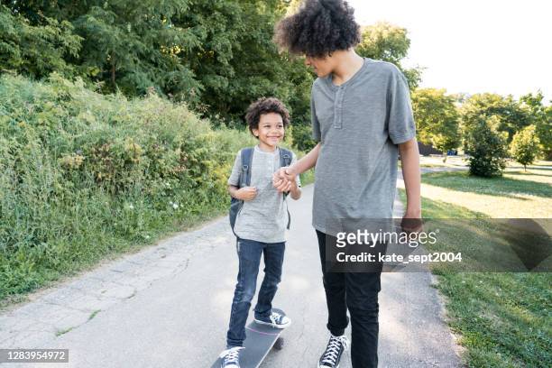 young man holding hand while helping smiling brother balancing on skateboard at park - sibling stock pictures, royalty-free photos & images