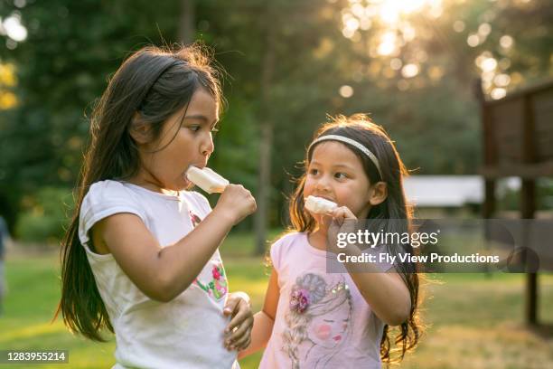 hermanas hispanas comiendo paletas en una calurosa tarde de verano - de descendencia mixta fotografías e imágenes de stock