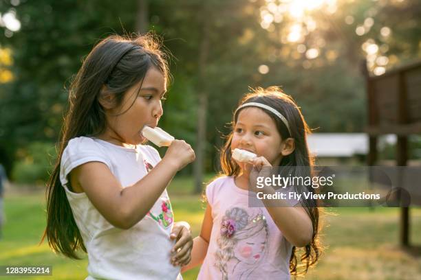 hispanic sisters eating popsicles on a hot summer afternoon - child eating outdoors stock pictures, royalty-free photos & images
