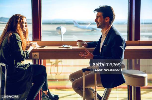 happy business couple discussing while sitting at airport cafe - wartehalle stock-fotos und bilder