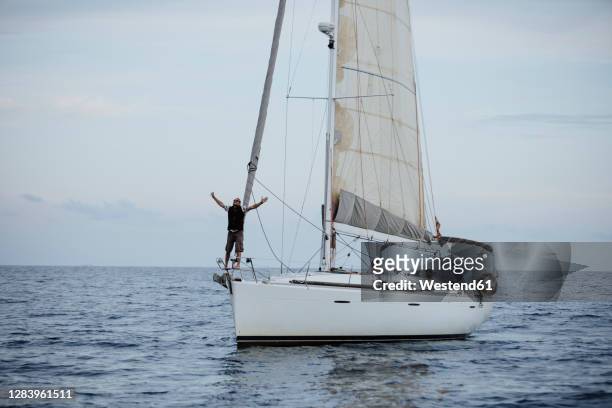 female sailor with arms raised standing on sailboat in sea - sailor arm stock-fotos und bilder