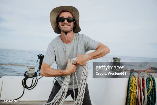 smiling sailor wearing sunglasses and hat holding ropes in sailboat - man sunglasses stock pictures, royalty-free photos & images