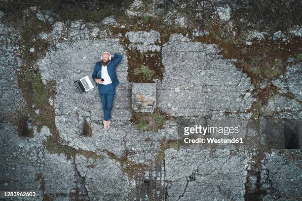 aerial view of businessman wearing suit listening music while lying on land in forest - headphones isolated ストックフォトと画像